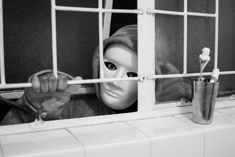 Close-up portrait of burglar wearing mask peeking through window