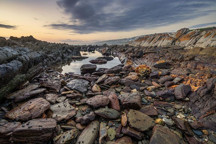 Scenic view of drained rock pool against sky during sunset and low tide