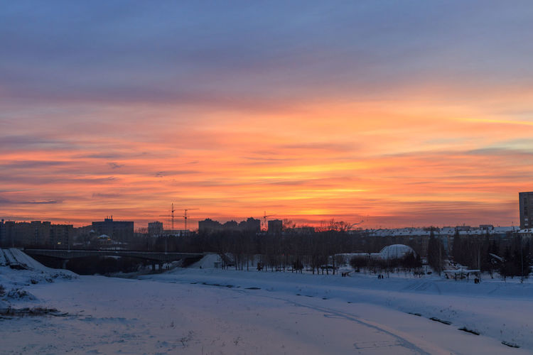 Snow covered field against sky during sunset
