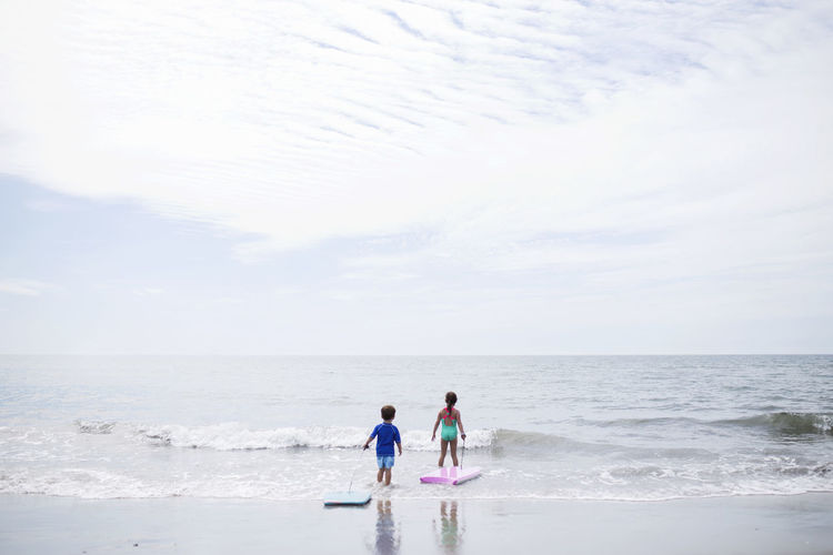 Scenic view of children wading into sea against sky