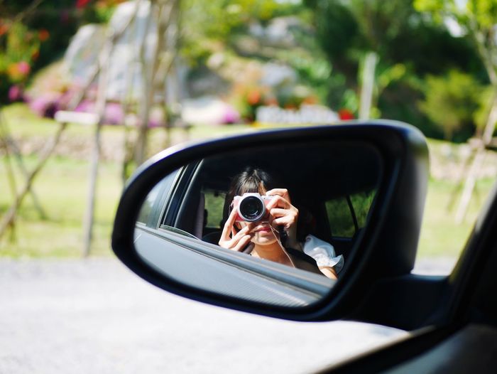 Reflection of woman photographing in side-view mirror