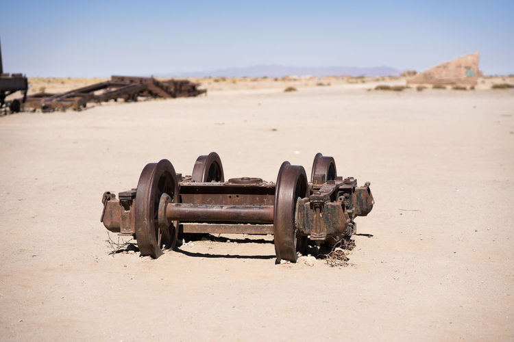 Close-up of old machinery on sand against clear sky