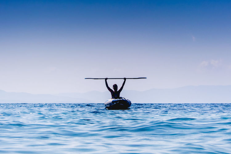 Woman holding oar moving in boat on sea against sky