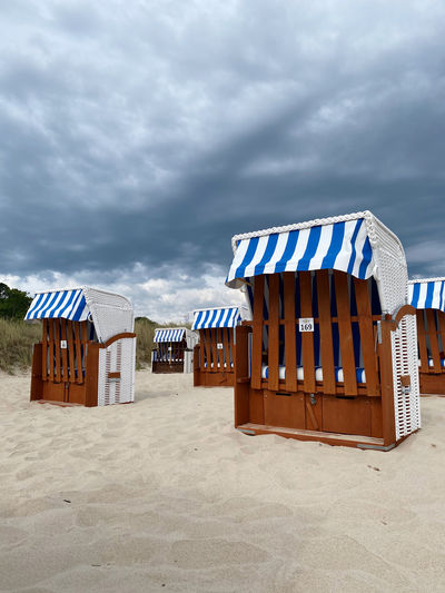 Hooded beach chairs on sand against sky