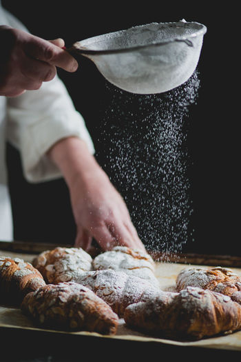 Midsection of chef sprinkling powdered sugar on croissants in bakery