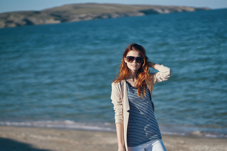 Portrait of young woman wearing sunglasses standing on beach