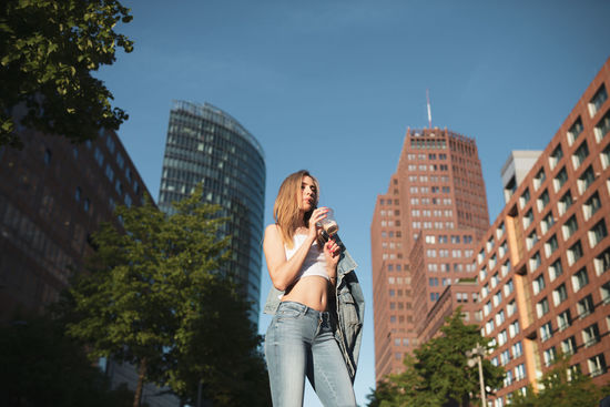Low angle view of woman drinking coffee against buildings