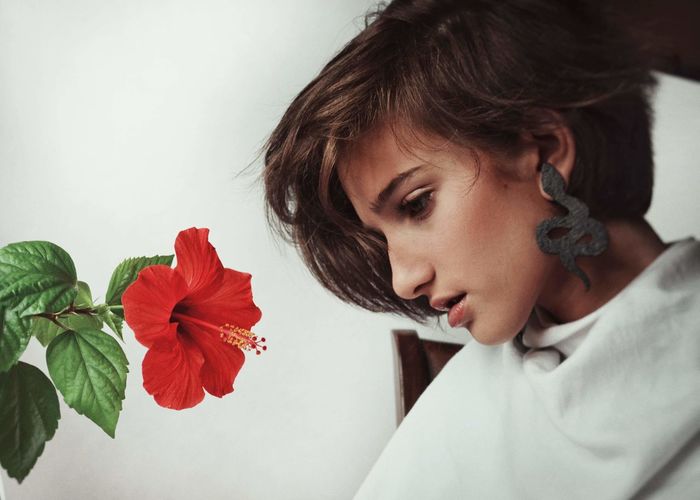 Side view of thoughtful young woman by red hibiscus at home