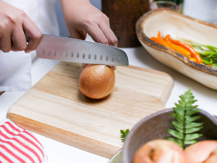 Cropped hands of chef cutting onion on table