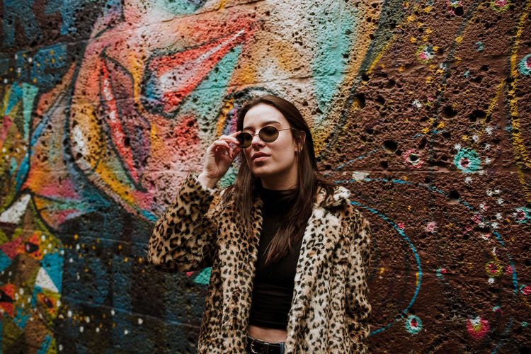 Young woman in sunglasses standing against graffiti wall