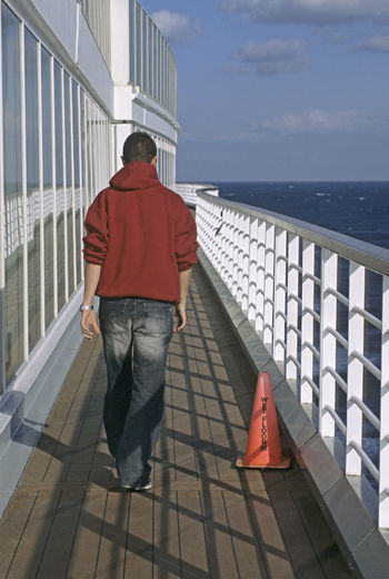 Rear view of man on railing by sea against sky