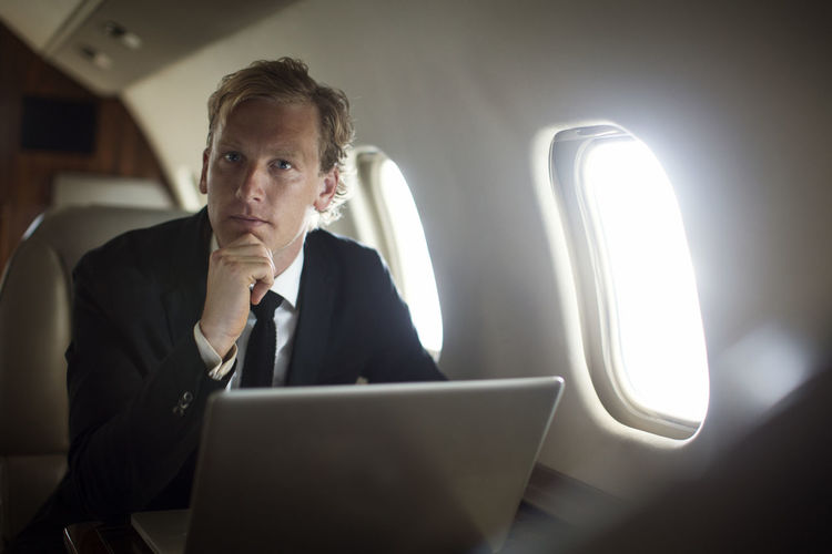 Portrait of confident businessman sitting with laptop in airplane