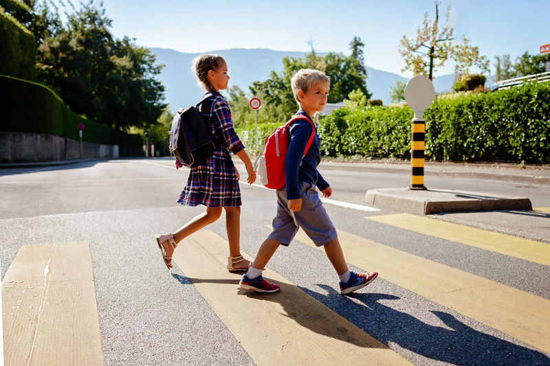 Kids with backpacks cross the road at crosswalk on the way to school. child safety, education