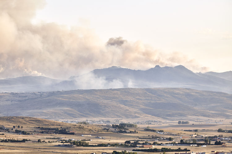 Photograph of a large forest fire with a large column of smoke on a hillside near a city