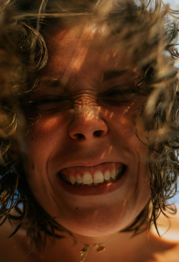 From below cheerful brown curly haired happy woman with closed eyes smiling at camera