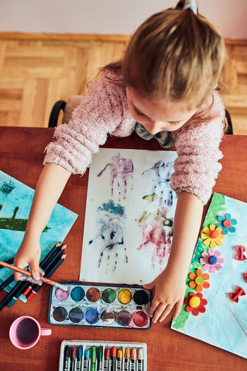 Little girl preschooler painting a picture using colorful paints and crayons. child having fun