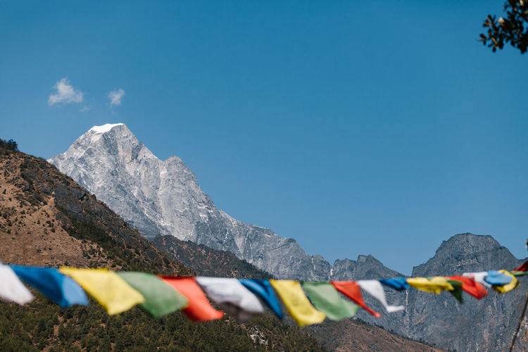 Traditional colorful prayer flags hanging on rope against rocky mountains and blue sky in sunny day