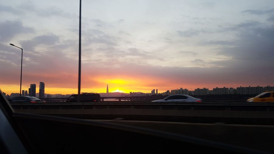 Cars on road in city against sky during sunset