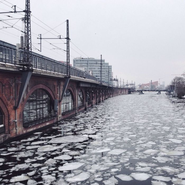 Frozen river by bridge against clear sky