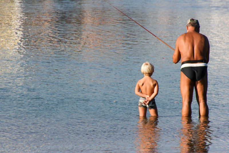 Rear view of a senior man and a boy fishing in water