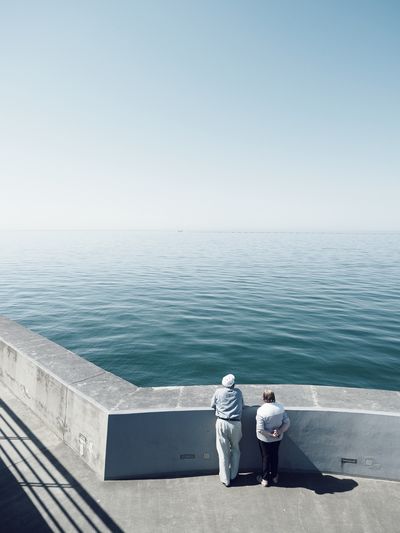 Rear view of men looking at sea against clear sky