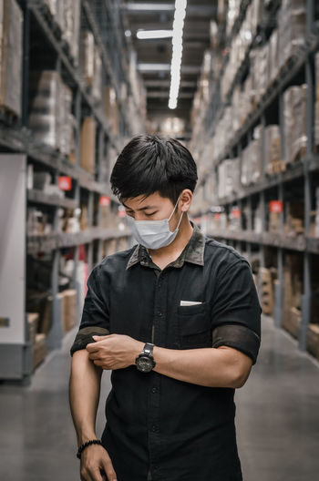 Young man looking away while standing in building with face mask