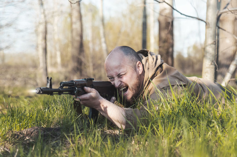 Man with rifle lying on grass in forest
