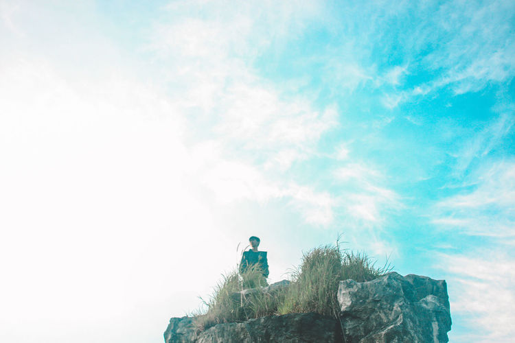 Low angle view of person on rock against sky