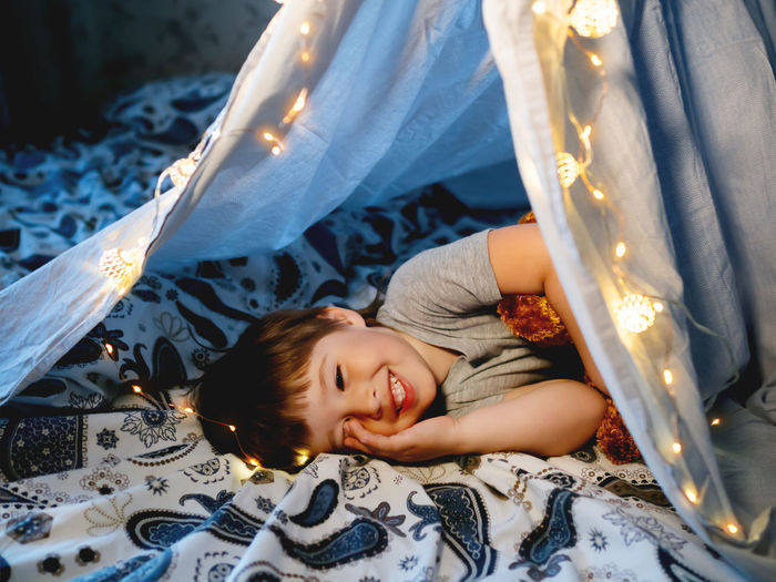 Little boy plays with his teddy bear. toddler lying in tent made of linen sheet on bed.diy interior.