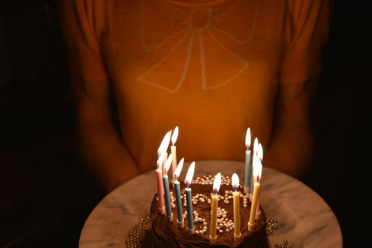 Midsection of woman holding illuminated birthday cake