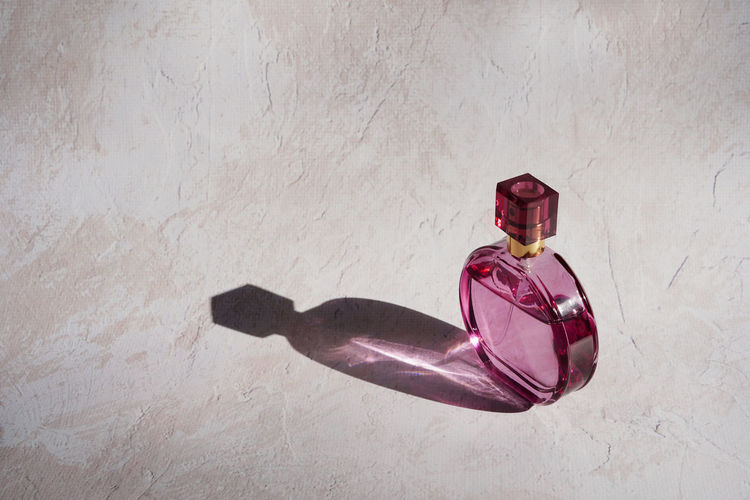 Pink perfume bottle with reflection and contrasting shadow on concrete background