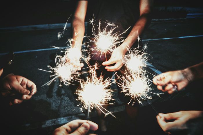 Cropped image of people holding sparklers while standing outdoors at night