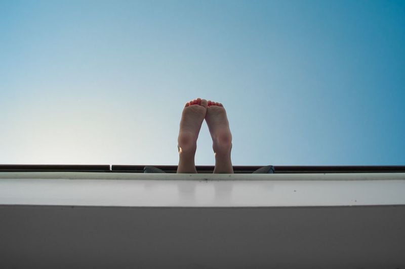 Low angle view of feet hanging against clear blue sky