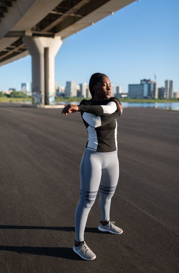 African american sportswoman warming up under bridge