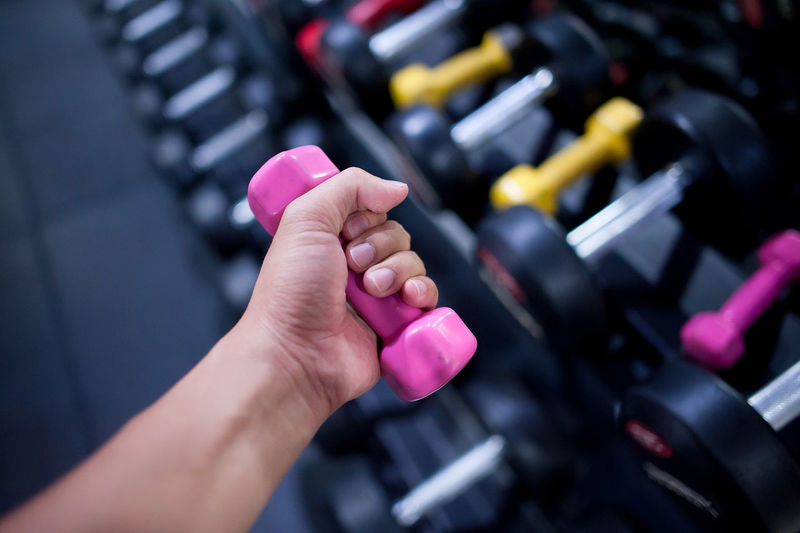 Cropped hand of men lifting dumbbell in gym