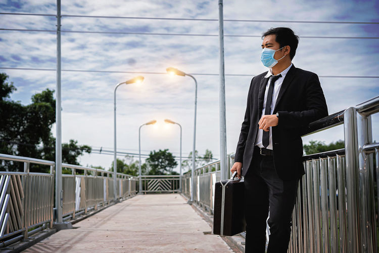 Asian businessman holding briefcase walking on overpass looking outside