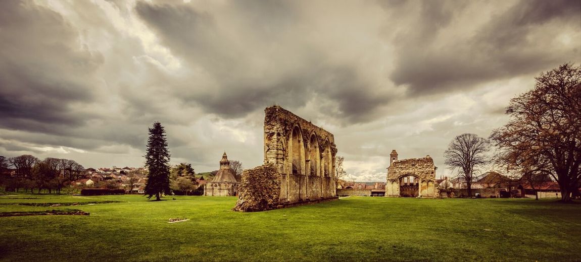 Old ruins on grassy field against cloudy sky