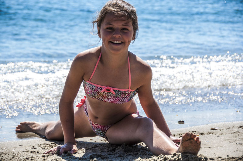 Portrait of smiling girl doing splits at beach on sunny day
