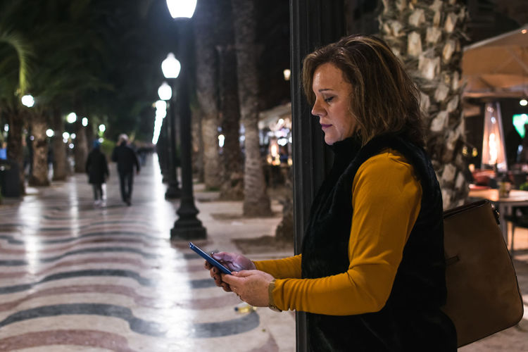 Middle-age woman is watching her smartphone on the street