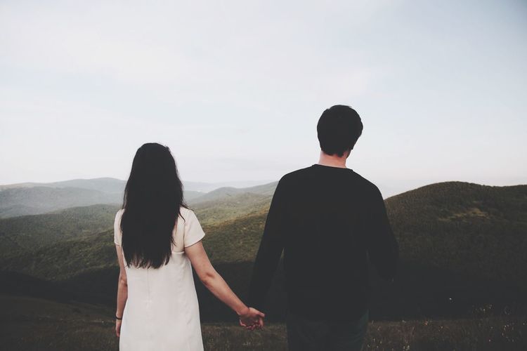 Young couple holding hands and looking at scenic view in mountains