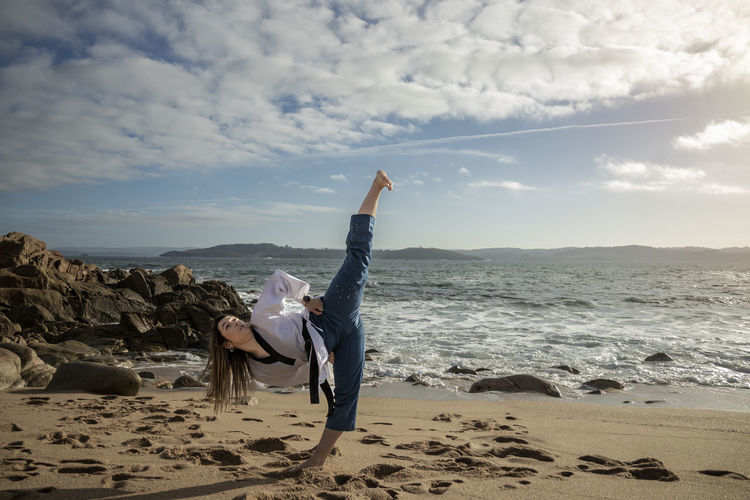 Woman doing taekwondo on the beach giving a kick to the air