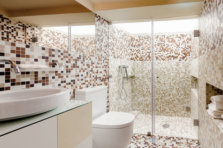 Interior of a modern bathroom decorated with brown tiles with a large shower cabin