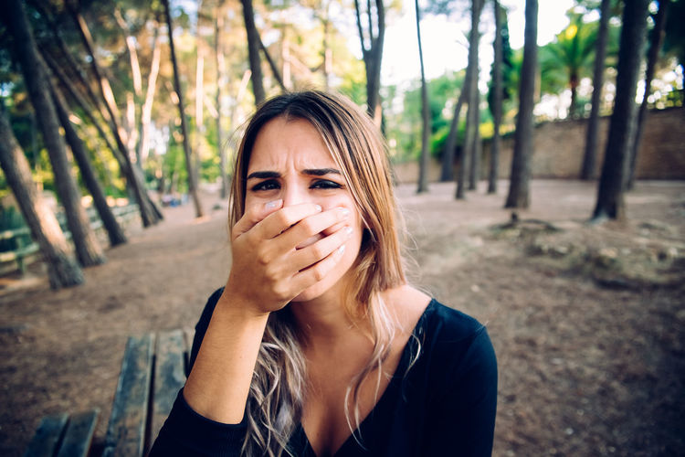 Portrait of young woman covering mouth in forest
