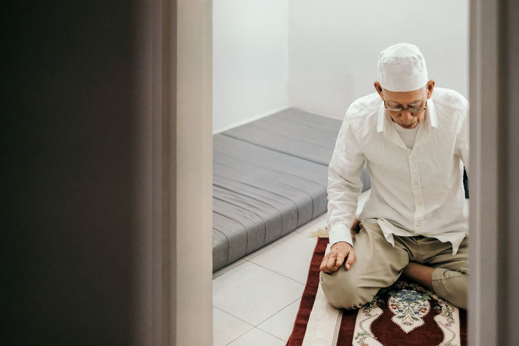 Senior man praying at home seen through doorway