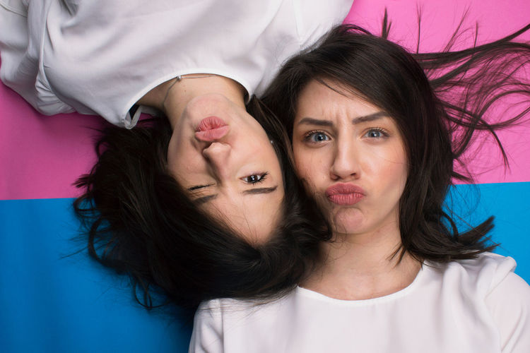 Directly above shot of female friends puckering while lying on colored background