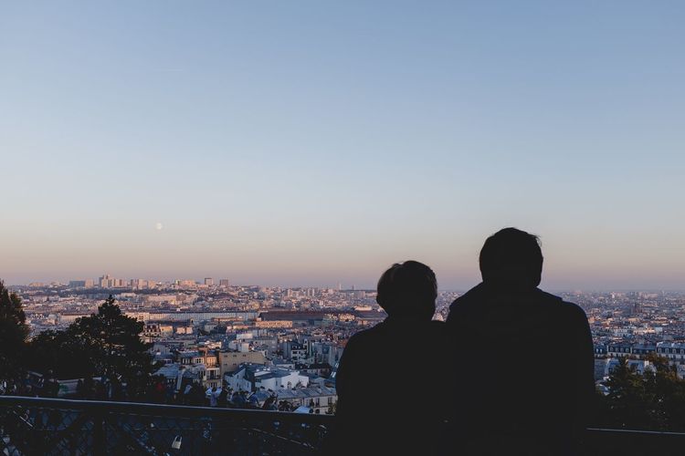 Rear view of man and woman looking at cityscape against sky