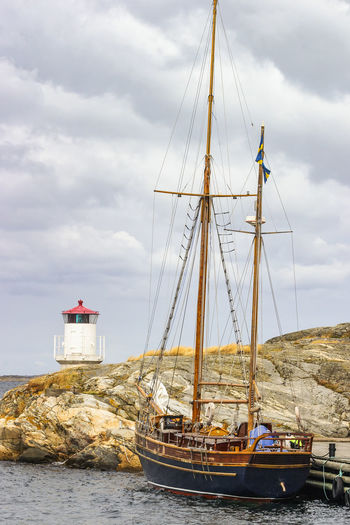 Old wooden ship and a lighthouse on a rocky coast