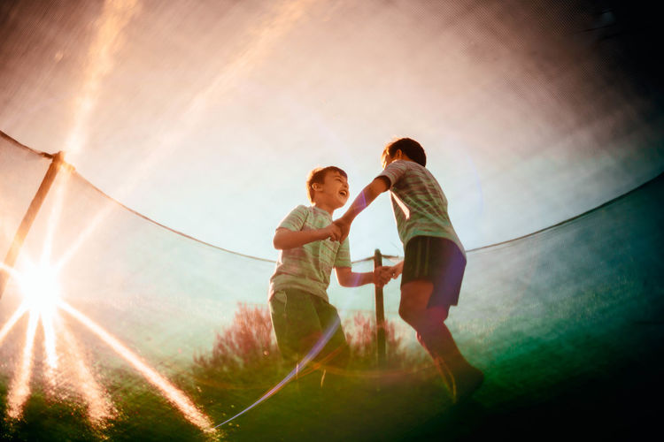 Low angle view of happy siblings holding hands while playing against sky