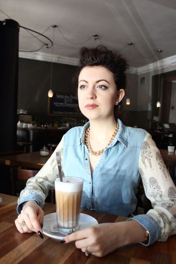 Thoughtful young woman with frothy drink looking away while sitting at cafe