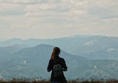 Rear view of woman standing on land against mountains and sky